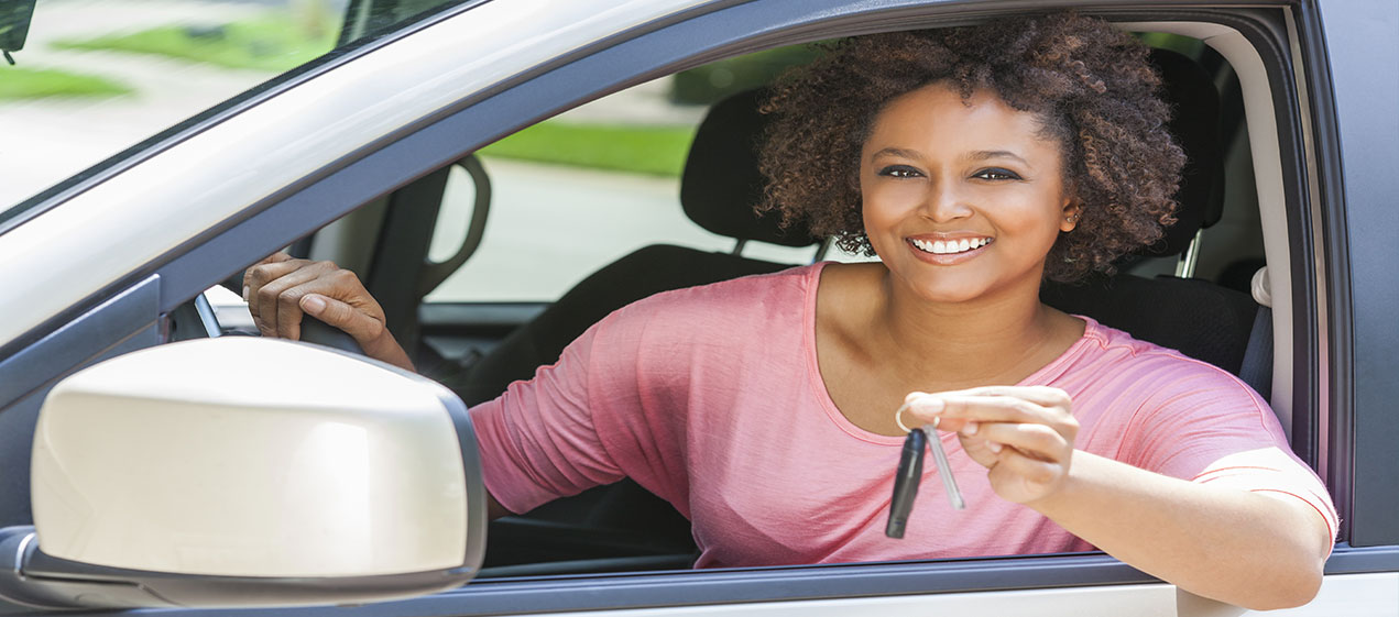 smiling African American female in car with arm out the window holding a set of keys