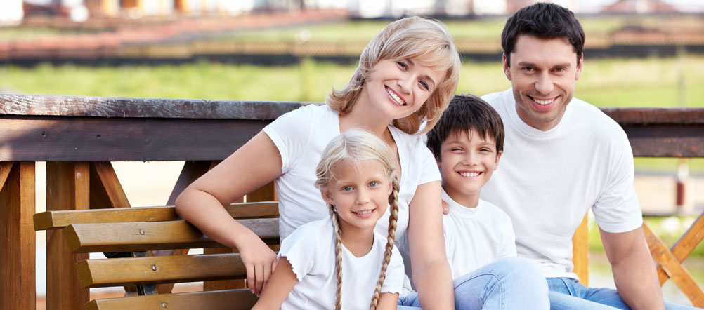 Young happy family is sitting on a bench together on a dock over the water.