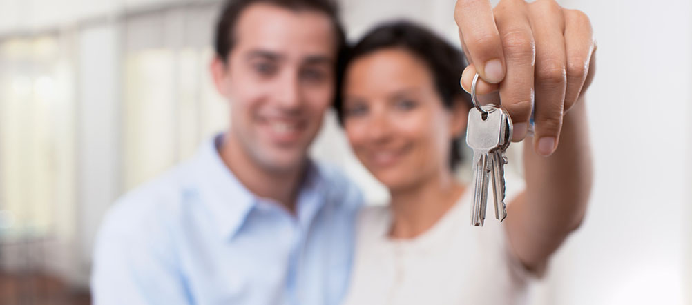 A happy couple is holding up a set of house keys. 